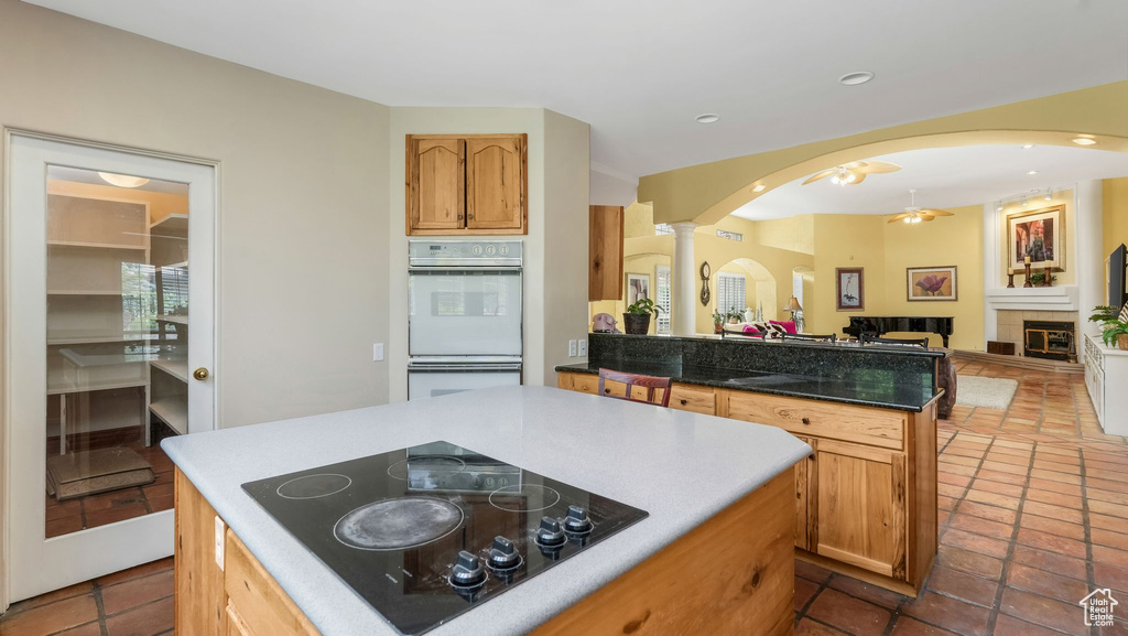 Kitchen featuring black electric stovetop, double oven, decorative columns, arched walkways, and a peninsula