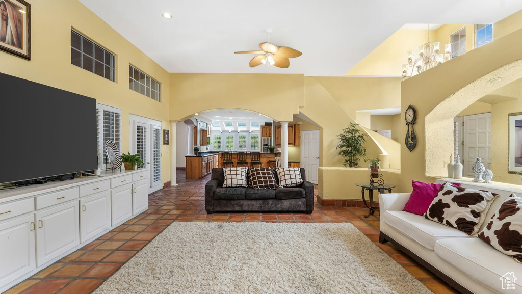 Living area featuring arched walkways, decorative columns, ceiling fan, a towering ceiling, and tile patterned floors