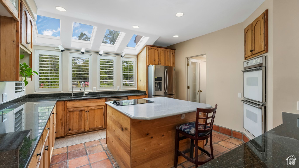 Kitchen featuring stainless steel refrigerator with ice dispenser, double oven, a skylight, light tile patterned floors, and recessed lighting