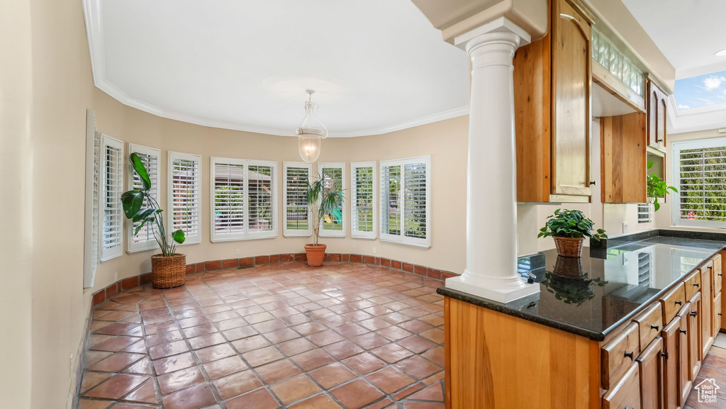 Kitchen featuring decorative columns, tile patterned flooring, ornamental molding, hanging light fixtures, and brown cabinetry