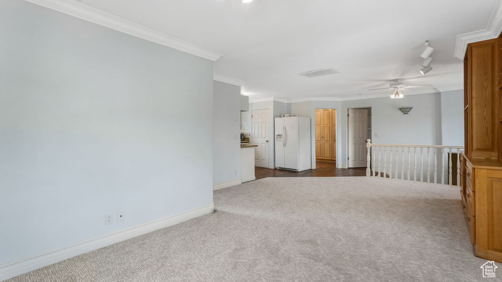 Spare room featuring dark colored carpet, crown molding, and ceiling fan
