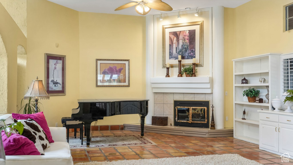 Living room with track lighting, ceiling fan, tile patterned flooring, and a tiled fireplace