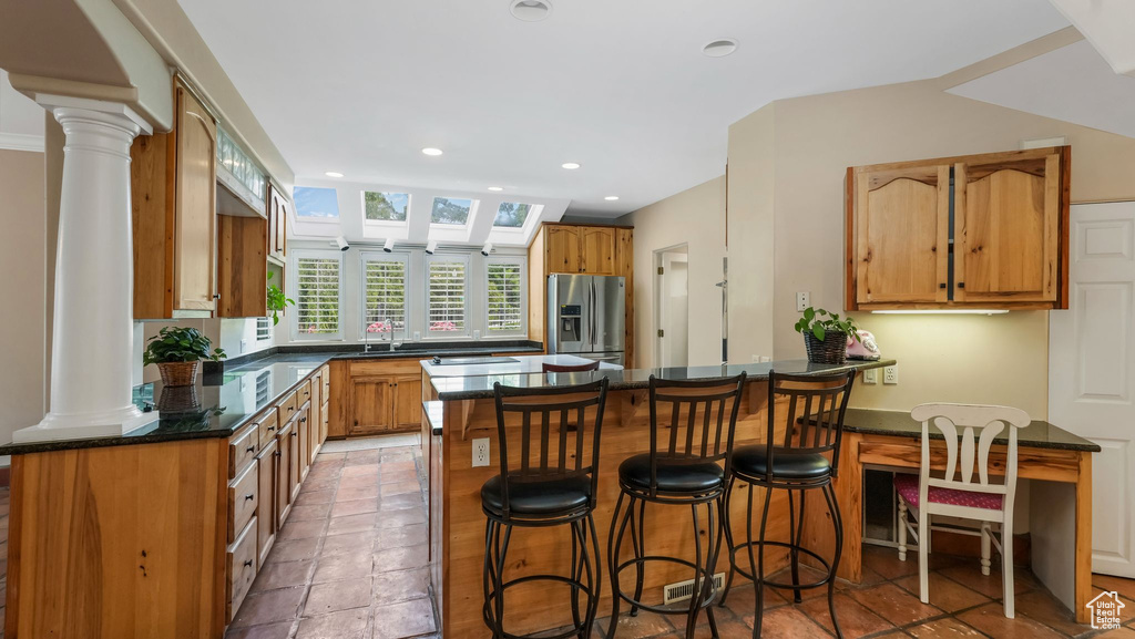 Kitchen featuring stainless steel fridge, a peninsula, decorative columns, recessed lighting, and a kitchen breakfast bar