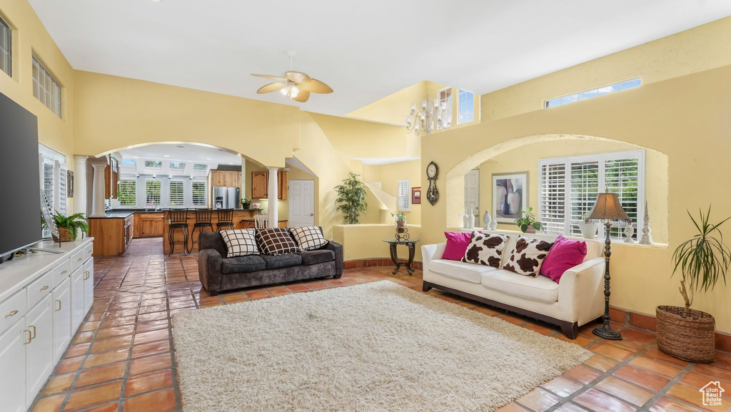 Tiled living room with ornate columns, arched walkways, a ceiling fan, and a high ceiling