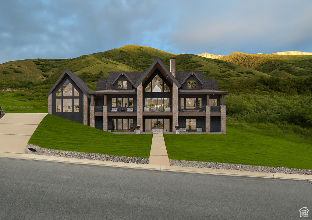 View of front of property featuring a chimney, a front yard, a balcony, and a mountain view