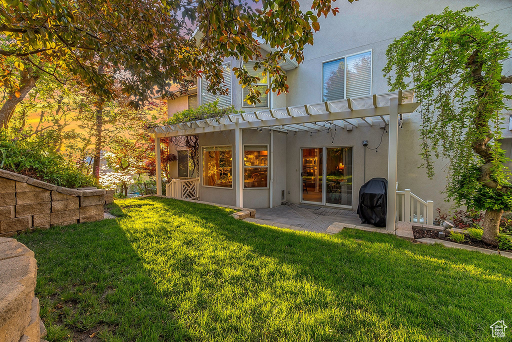 Rear view of house with stucco siding, a pergola, and a yard