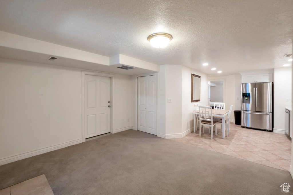 Basement with stainless steel refrigerator with ice dispenser, a textured ceiling, light colored carpet, recessed lighting, and light tile patterned floors