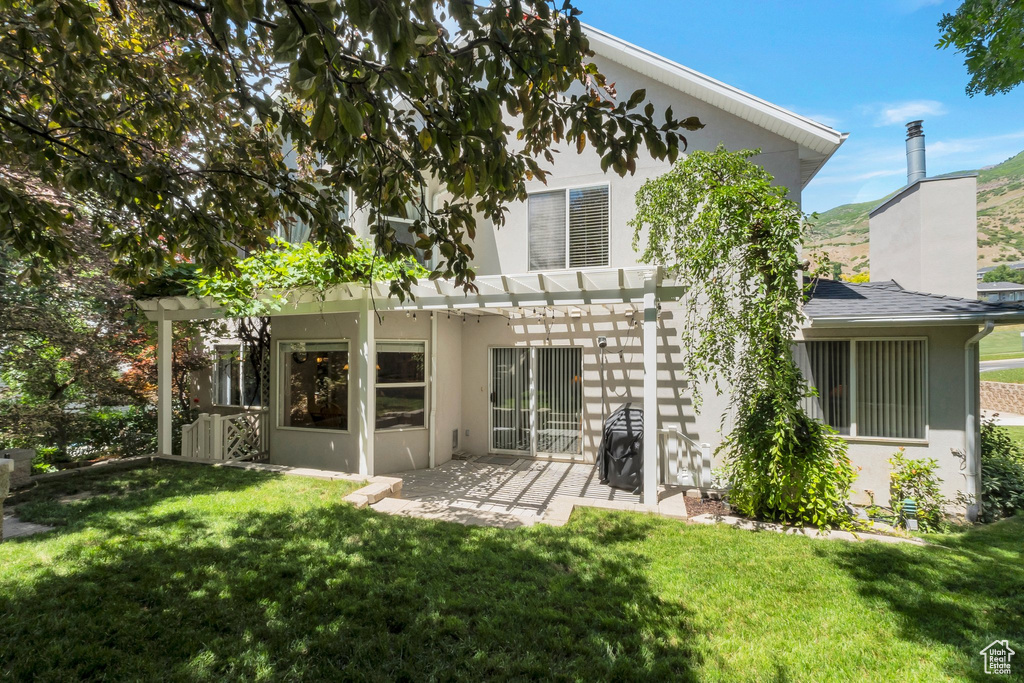 Rear view of property with a pergola, stucco siding, a patio area, a yard, and a chimney