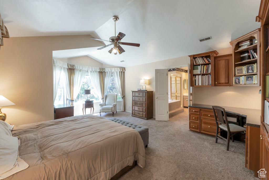Bedroom with vaulted ceiling, light colored carpet, built in desk, ensuite bath, and ceiling fan
