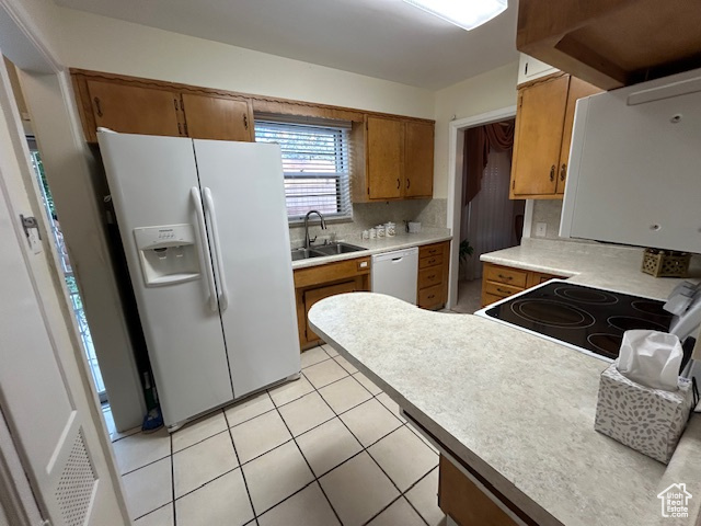 Kitchen with white appliances, brown cabinetry, light countertops, backsplash, and light tile patterned floors