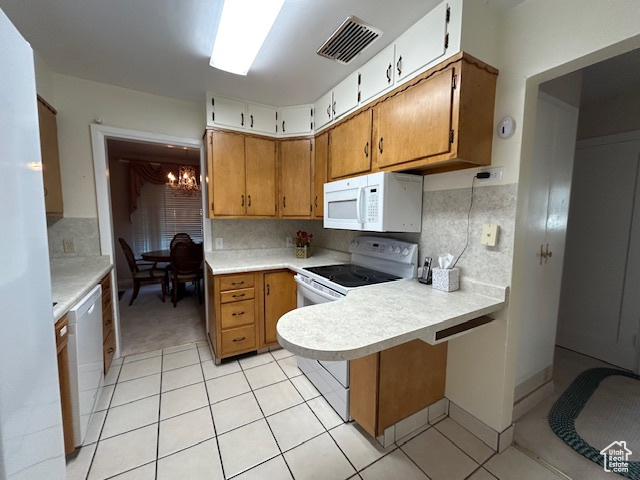 Kitchen featuring white appliances, light countertops, light tile patterned floors, a peninsula, and a chandelier