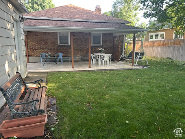Back of house featuring brick siding, a chimney, roof with shingles, and a patio area