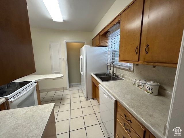 Kitchen featuring white appliances, brown cabinetry, light tile patterned flooring, and light countertops