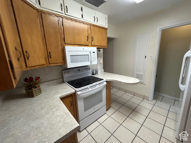 Kitchen with white appliances, light countertops, light tile patterned floors, and brown cabinetry
