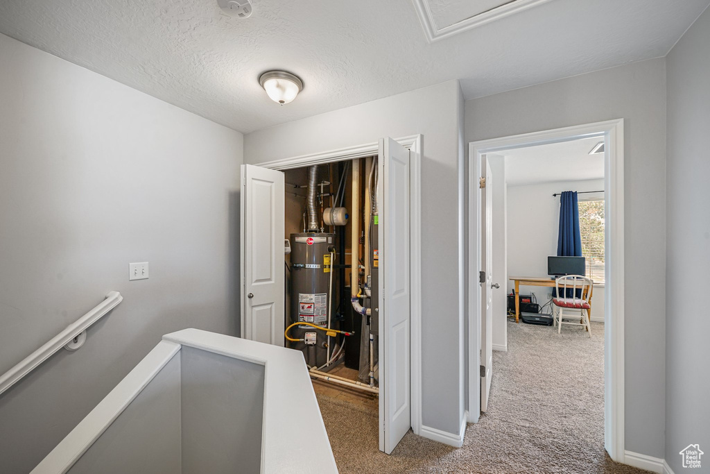 Hallway with strapped water heater, carpet floors, an upstairs landing, and a textured ceiling