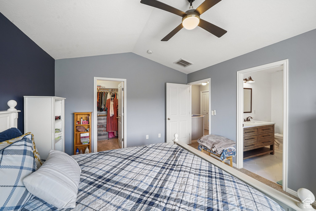 Carpeted bedroom featuring a walk in closet, lofted ceiling, a closet, ensuite bath, and a ceiling fan