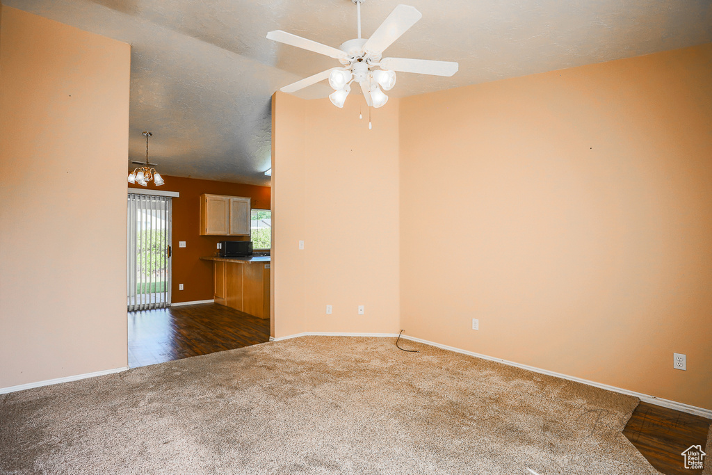 Unfurnished living room featuring dark colored carpet, a ceiling fan, and a chandelier