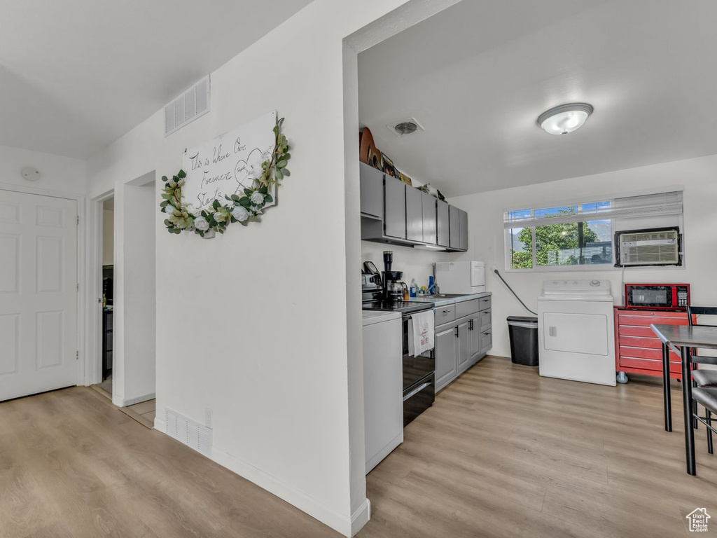 Kitchen with washer / clothes dryer, light wood finished floors, black range with electric cooktop, a wall unit AC, and gray cabinetry