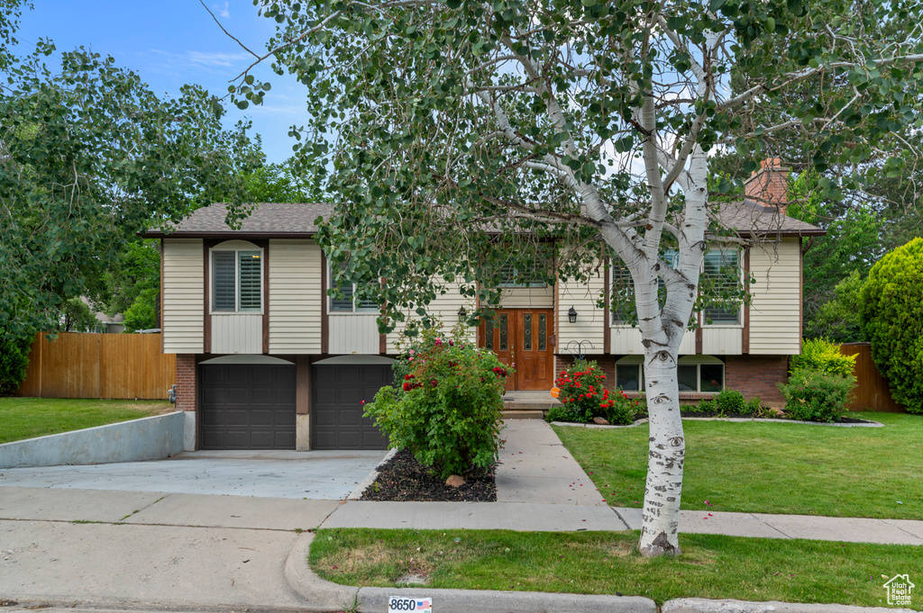 Raised ranch featuring driveway, brick siding, a garage, a shingled roof, and french doors