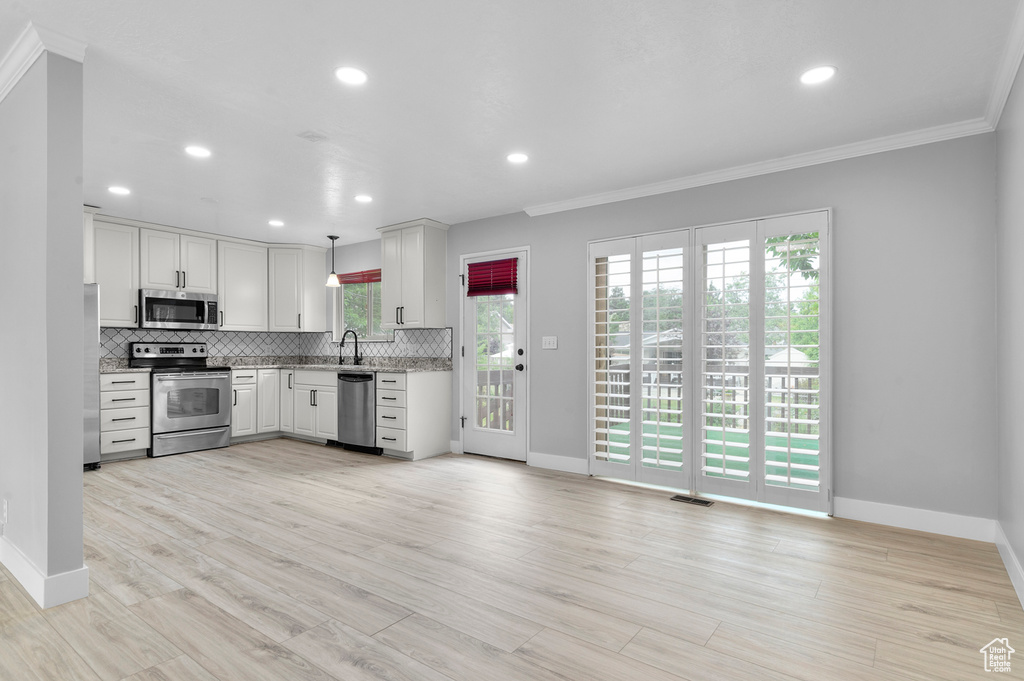 Kitchen featuring stainless steel appliances, crown molding, backsplash, white cabinetry, and recessed lighting