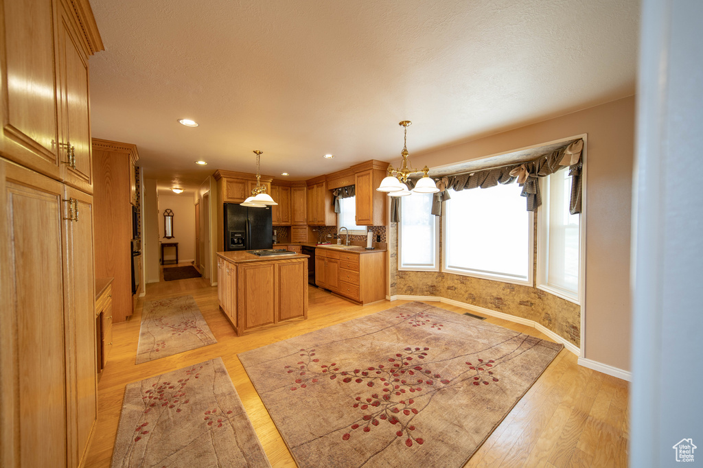 Kitchen featuring black appliances, light wood-type flooring, a center island, hanging light fixtures, and recessed lighting