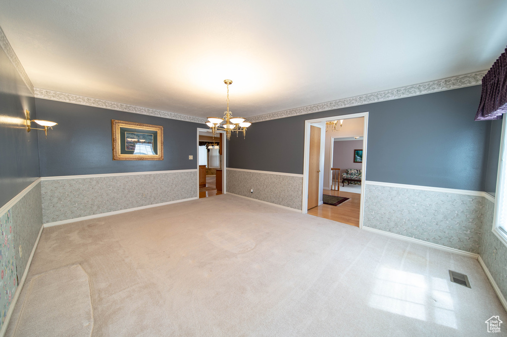 Unfurnished room with a chandelier, wallpapered walls, carpet, and a wainscoted wall