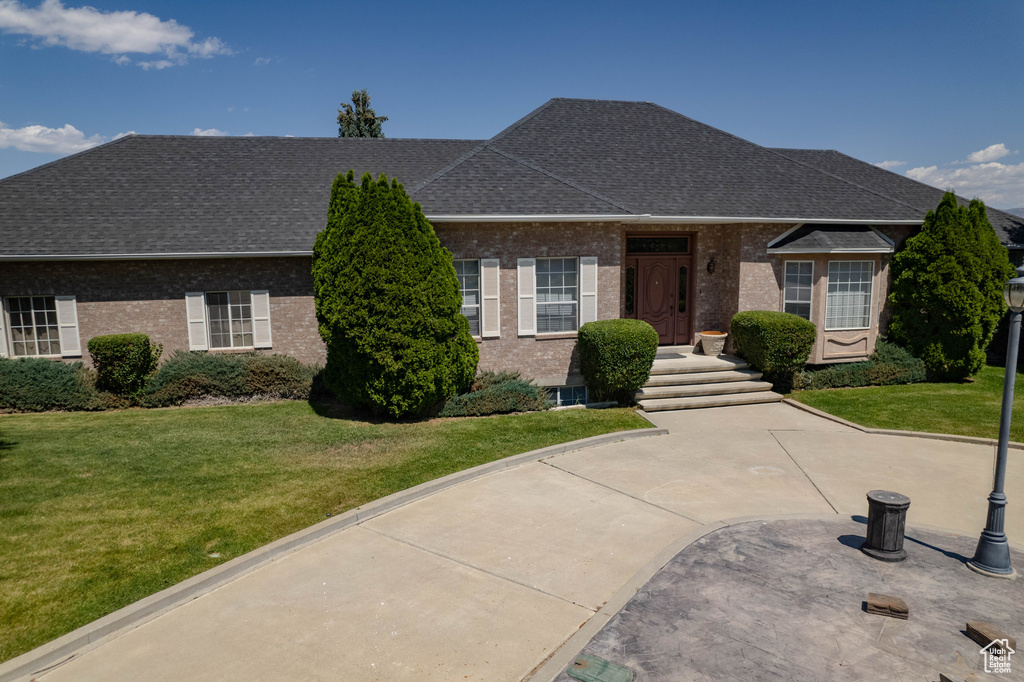 View of front of home featuring brick siding, a front lawn, and roof with shingles