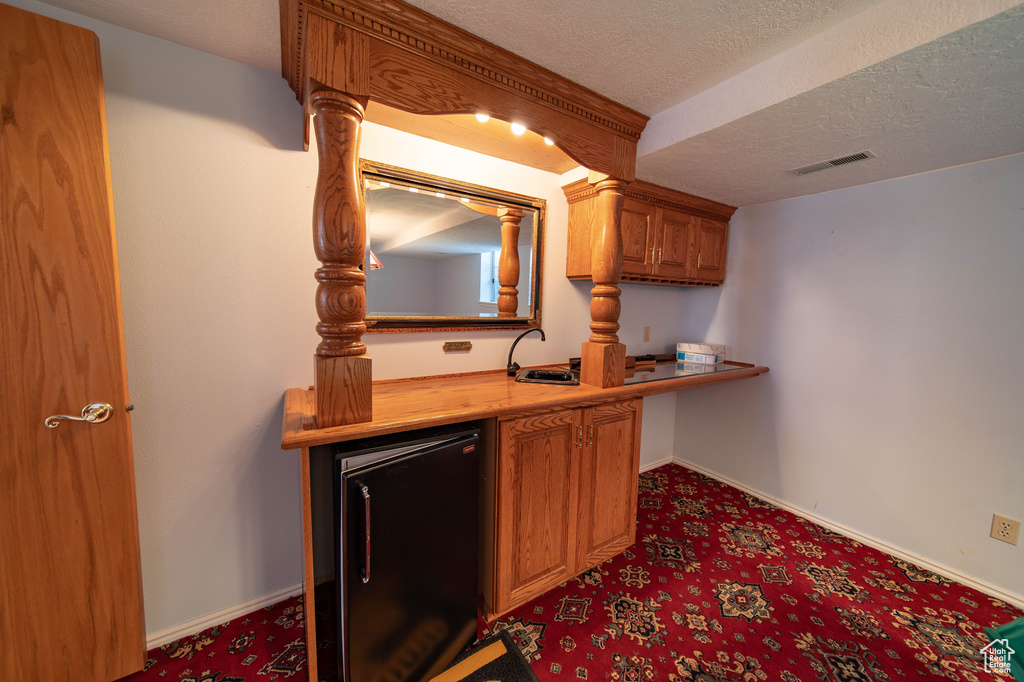 Indoor bar with fridge, carpet, and a textured ceiling