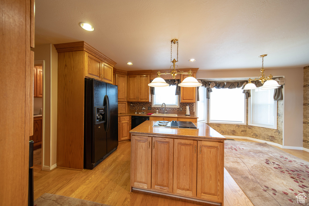Kitchen featuring black appliances, light wood-style flooring, a kitchen island, a chandelier, and tasteful backsplash