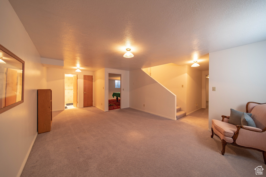 Unfurnished living room featuring stairs, light colored carpet, and a textured ceiling