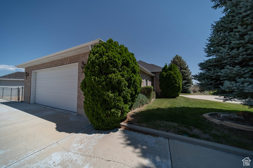 View of property exterior featuring a yard, brick siding, a garage, and concrete driveway