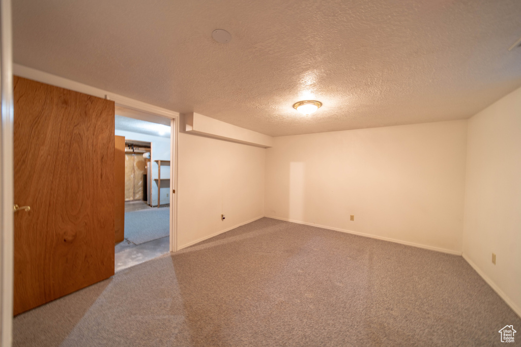 Carpeted spare room featuring a textured ceiling and baseboards