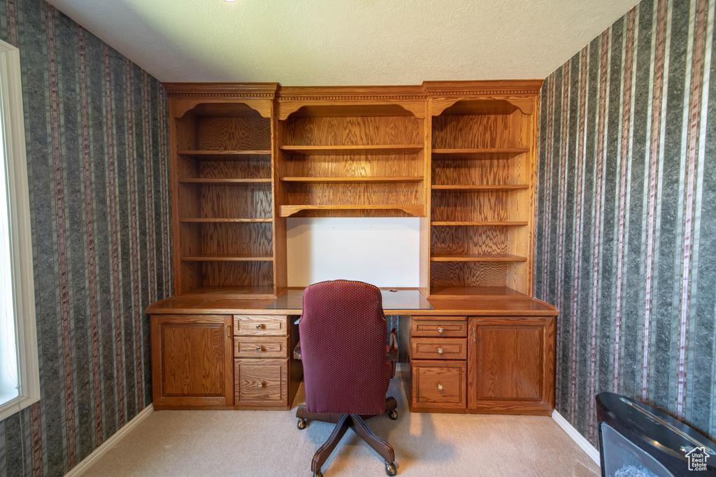 Home office with wallpapered walls, built in desk, and light colored carpet