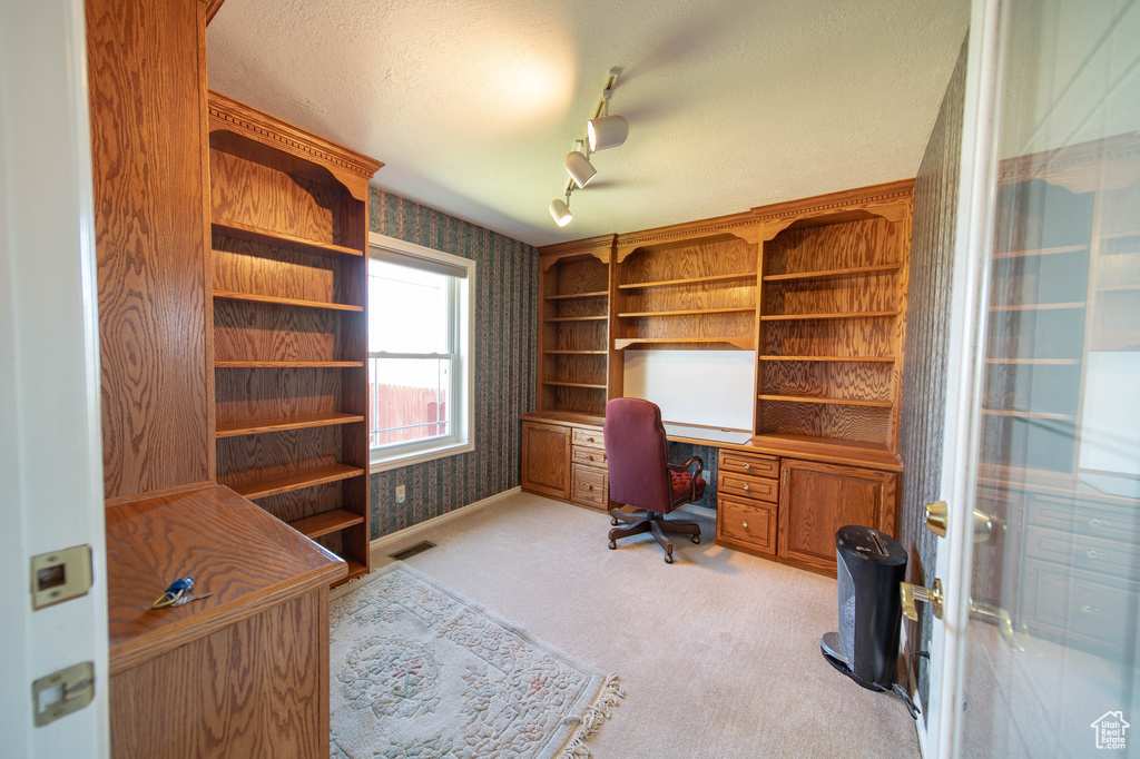Office space with wallpapered walls, light carpet, rail lighting, and a textured ceiling