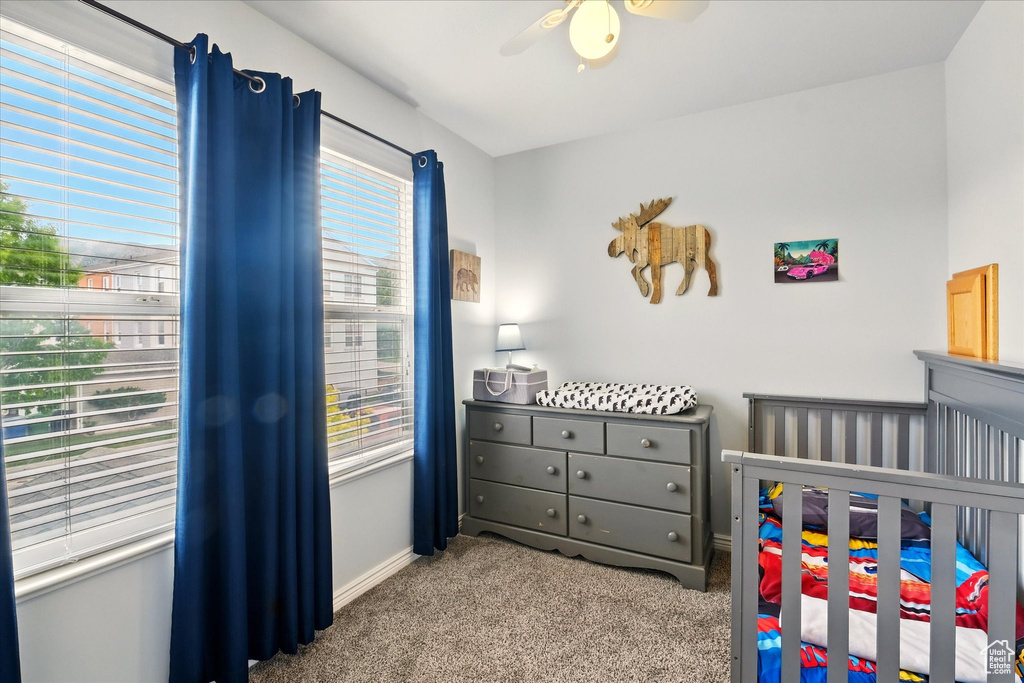 Carpeted bedroom featuring a nursery area and ceiling fan