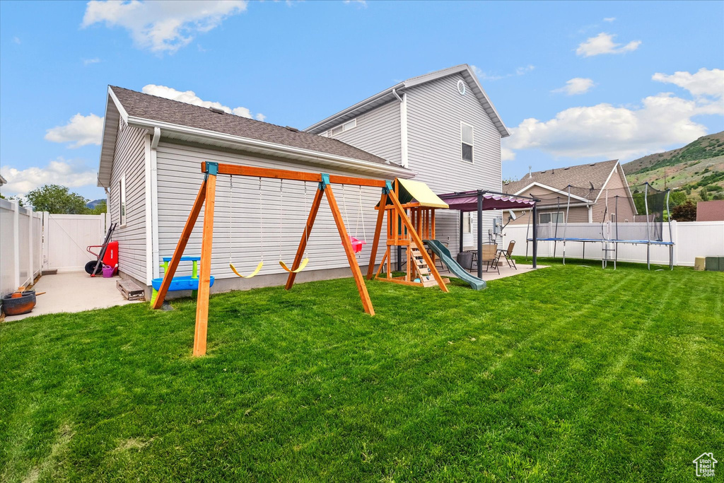 Fenced backyard with a trampoline, a patio area, and a playground