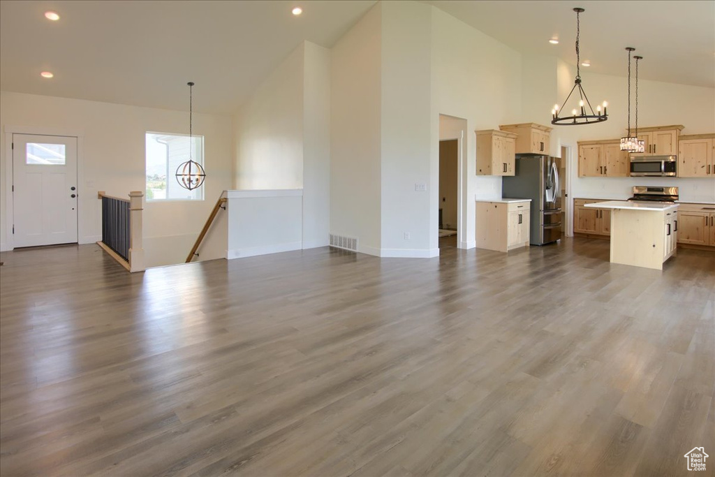 Unfurnished living room featuring a chandelier, high vaulted ceiling, recessed lighting, and dark wood-style flooring