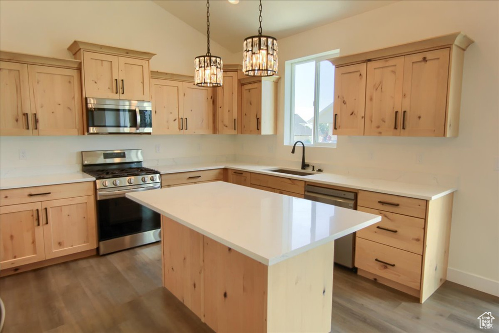 Kitchen with appliances with stainless steel finishes, light brown cabinets, wood finished floors, light countertops, and a chandelier