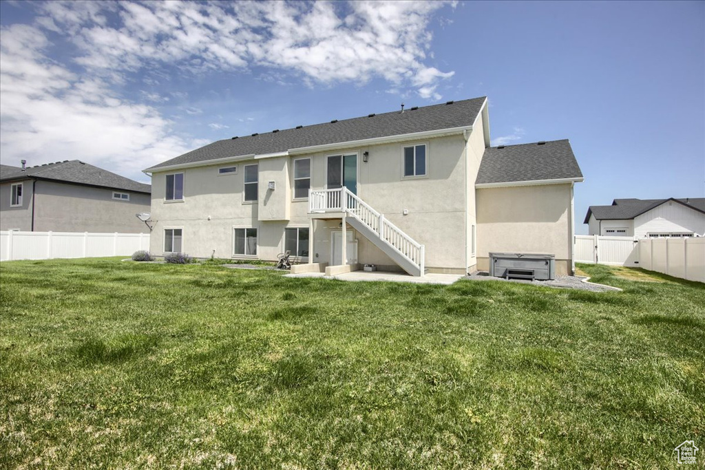 Rear view of property featuring a hot tub, a fenced backyard, stucco siding, and a patio