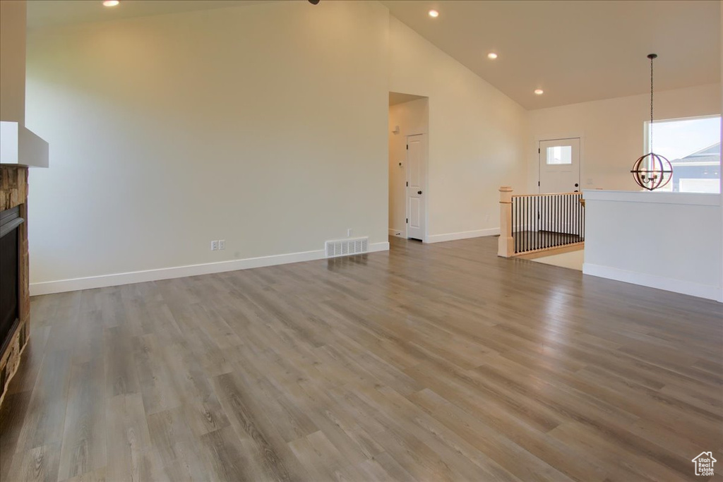Unfurnished living room featuring a chandelier, recessed lighting, wood finished floors, high vaulted ceiling, and a stone fireplace