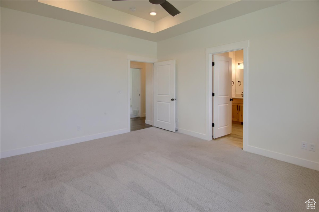 Unfurnished bedroom with light carpet, a tray ceiling, and connected bathroom