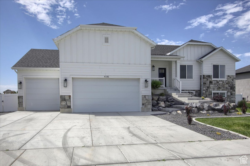 View of front of house with board and batten siding, stone siding, a garage, concrete driveway, and a shingled roof