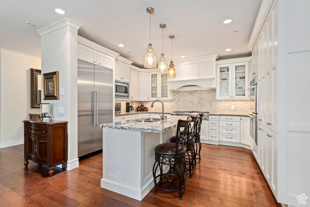 Kitchen with built in appliances, backsplash, light stone counters, glass insert cabinets, and recessed lighting