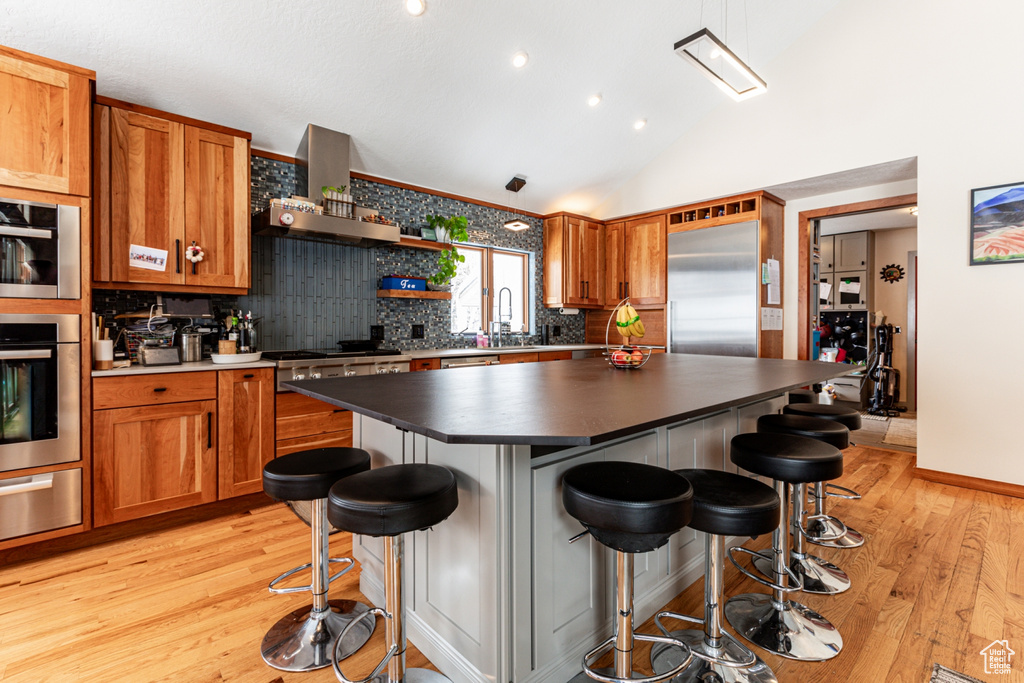 Kitchen featuring extractor fan, appliances with stainless steel finishes, light wood finished floors, a warming drawer, and dark countertops