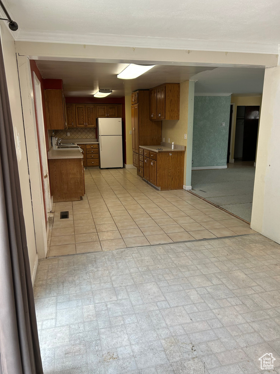 Kitchen with freestanding refrigerator, ornamental molding, brown cabinetry, backsplash, and light countertops
