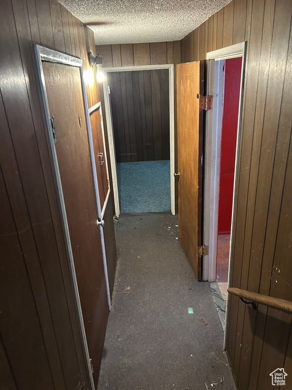 Corridor featuring carpet flooring, wood walls, and a textured ceiling