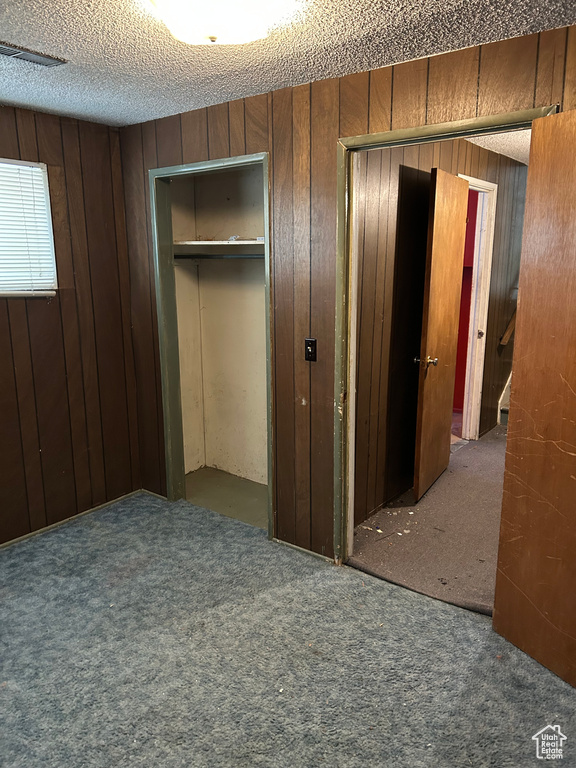 Unfurnished bedroom featuring carpet flooring, wood walls, and a textured ceiling