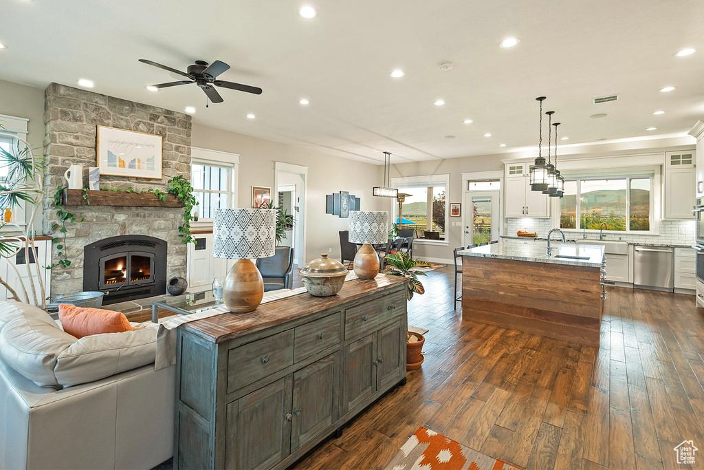 Living room featuring a ceiling fan, dark wood finished floors, a stone fireplace, and recessed lighting