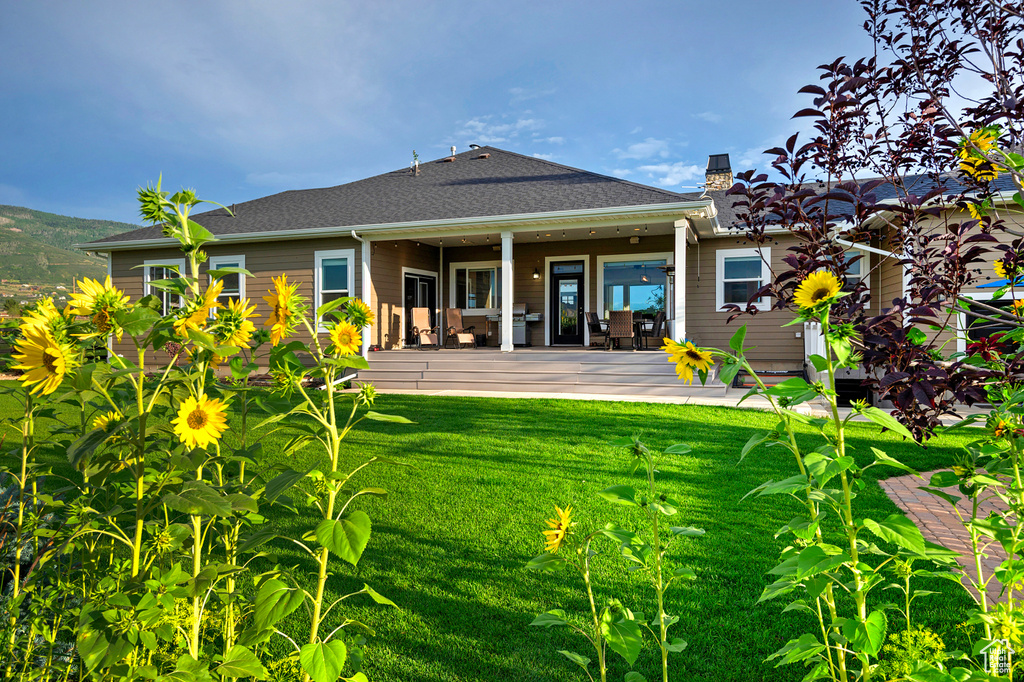 Back of house featuring a lawn, a chimney, a patio, and a shingled roof