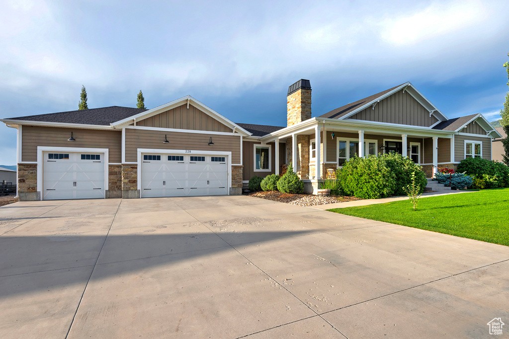Craftsman-style house featuring board and batten siding, concrete driveway, a garage, a chimney, and a porch